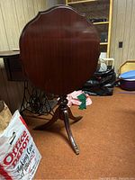 Front view of round flip top wood table showing tabletop and base with three legs