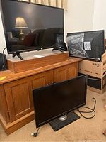 Photo showing three TVs: 27-inch LG on wooden stand on a cabinet, 22-inch Samsung TV on floor, 32-inch Samsung TV leaning against boxes.