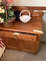 Front view of vintage wooden cabinet showing two doors, top drawer partially open with keys hanging, objects on top including a flower basket, white ceramic basket, and dark blue container.