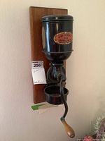 Front view of vintage wall-mounted coffee grinder showing label 'Universal 014 Coffee Mill' and wooden handle attached to the metal body.