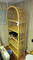 Full view of tall wicker shelf unit placed in basement corner, showing its height and four shelves.