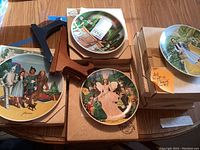 Photo showing multiple Wizard of Oz collectible plates with colorful character illustrations and three wooden plate stands scattered among them.