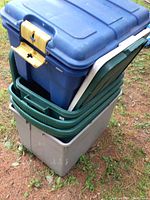 Stacked view of six assorted plastic totes showing blue, green, and gray colors with some lids included and one lid missing.