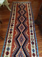 Full view of carpet runner showing central zigzag diamond patterns and border motifs in rust, navy, cream, light blue, and olive green on wooden floor.