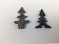 Front view of two small, ancient Bird Point arrowheads, one light brown and one black, laid side by side on white background.