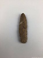 Top view of the brown stone spear point with catalog number attached, showing the detailed chipped flaked surface.