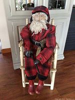 Full view of the antique handmade Adirondack mens hunting doll sitting in a chair, wearing a red and black plaid hunting outfit and red rubber boots.