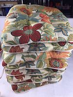 Stack of eight floral patterned chair cushions showing the top vibrant damask fabric with floral designs.