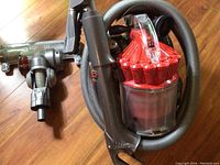 Dyson DC32 main vacuum unit with cyclone canister and connected hose laid on wooden floor