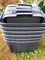 Stacked view of six dark blue Rubbermaid storage totes with lids, showing the exterior condition and size.