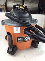 Ridgid orange and black wet/dry shop vacuum featuring handle, wheels, and hose attached to the unit.