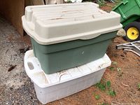 Two Rubbermaid jumbo totes stacked outdoors on a concrete surface with dirt and pine needles on lids and bases