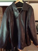Front view of vintage brown leather coat on hanger showing collar, shoulders and front zipper closure.