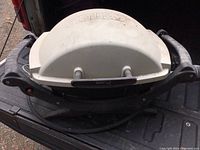 Top view of Weber portable propane grill with white lid and black handles placed inside a vehicle.