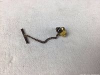 Tie tack with raw gold nugget on pin with screw back shown with attached chain and bar