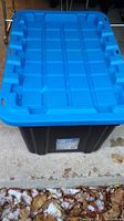 Closed blue-lidded black plastic storage bin showing textured lid design