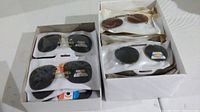 Box containing multiple pairs of polarized sunglass clip-ons in various lens colors and styles, each in plastic packaging.