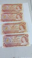 Four 1974 Canadian two dollar bills laid flat on white background, showing front side with Queen Elizabeth II portrait, creases on three bills, one crisp and crisp