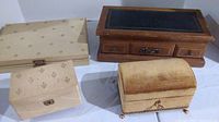 Four vintage jewelry boxes placed on a white surface; includes fabric and wooden boxes of various sizes and shapes.
