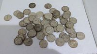 Top-down view of approximately sixty silver quarters scattered on white background