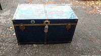 Front and side view of a dark blue metal trunk showing rust and locked latch.