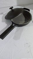 Black ceramic skillet with lid partially open showing gray interior and black exterior.
