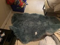 Blue shag rug visible on a beige carpeted floor with household items around it, showing texture and color of rug.