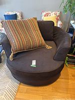Brown oversized tub armchair with large striped and brown cushions on it, showing rounded armrests and plush seating area.