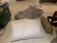 White standard pillow, olive green bolster pillow, and two gray square decorative pillows on beige carpet.
