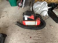 Overall view of the red and black Husky 2 gallon air compressor with coiled hose, sitting on garage floor.