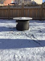 Full outdoor view of round fire pit table placed on snow-covered ground
