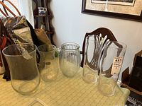Five clear glass vases with cylindrical and hourglass shapes on a table