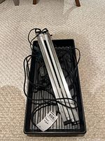 Grow light with three fluorescent tubes, power cords, and black plastic tray, all placed on beige carpet.