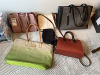 Top view of six ladies handbags including branded tote bags and crossbody bags in various colors and designs.