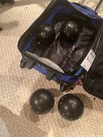 Four black lawn bowling balls inside and outside a blue wheeled carrying case on carpeted floor, showing the set includes balls and case.