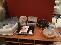 Wide view of multiple personal care items arranged on wooden shelves including Conair foot spa, Salter body composition analyzer, hair clippers case, and essential oil diffuser.