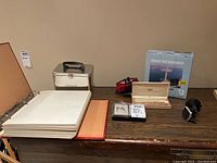 Overview of all items on a wooden surface showing photo album, TimBox metal case, puzzle box, pen case, radio, and phone mount.