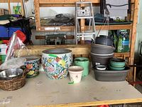 View of the large colorful ceramic planter with floral and butterfly designs, various smaller ceramic and resin planters, and a wicker basket-style planter on table.