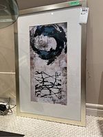 Framed print leaning against wall, showing full view with abstract design and light frame.