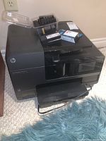 HP Officejet Pro 8620 printer with accessories and ink cartridges on top.