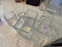 Four square clear glass vases and two cylindrical glass vases grouped on a surface