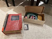 Overview of two deluxe stamp albums on carpet, next to a cardboard box with loose stamps and smaller stamp-related books.