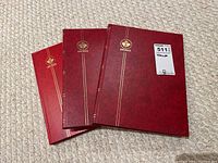 Photo showing three red Uni-Safe stamp albums stacked on carpeted floor.