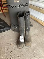 Front and side view of the tall men's green rubber boots with steel toes, showing dirt and scuffs on the surface, size label visible.