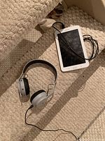 Samsung tablet with charging cord and House of Marley Rebel headphones placed on carpeted stairs
