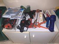 Lot overview showing various hand tools, power screwdriver, tube cutter, and two flashlights on top of white cabinet.