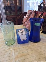 Three vases displayed on table: a tall green etched vase, a cobalt blue square vase, and a cobalt blue rounded vase.