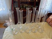 Ten clear glass stem vases arranged on a table, showcasing their shape and size; all are empty and intact.