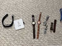 Photo of all watches and watch straps laid out on carpet. Includes Fitbit watch with manual, three ladies wrist watches, and three watch straps.