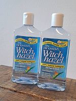 Two bottles of Dickinson's Witch Hazel 100% Natural Astringent for face and body in transparent plastic bottles with white flip-top caps.